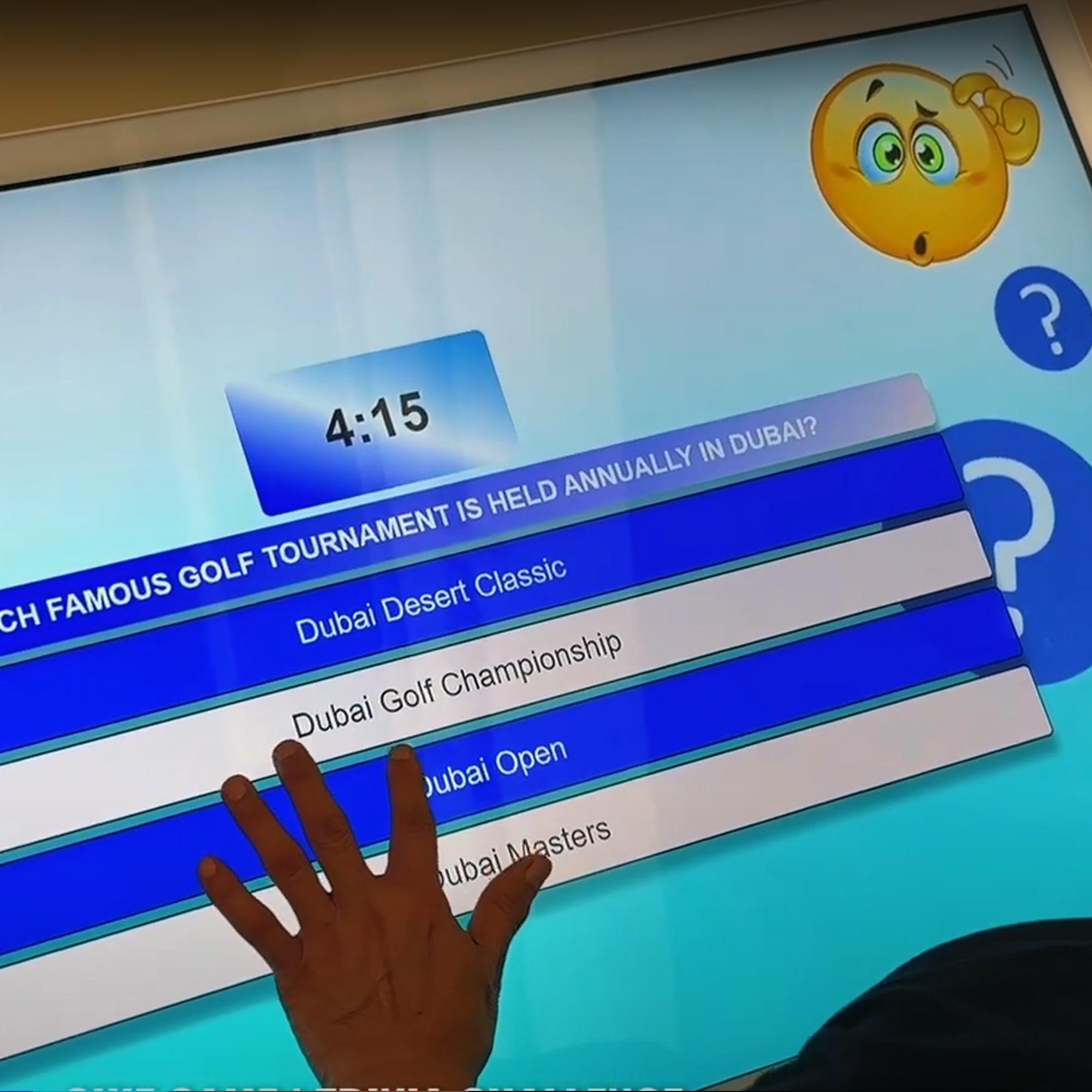 Touchscreen showing quiz results and a Dubai tower trivia question, with answer options and a person in a dark shirt standing beside the screen